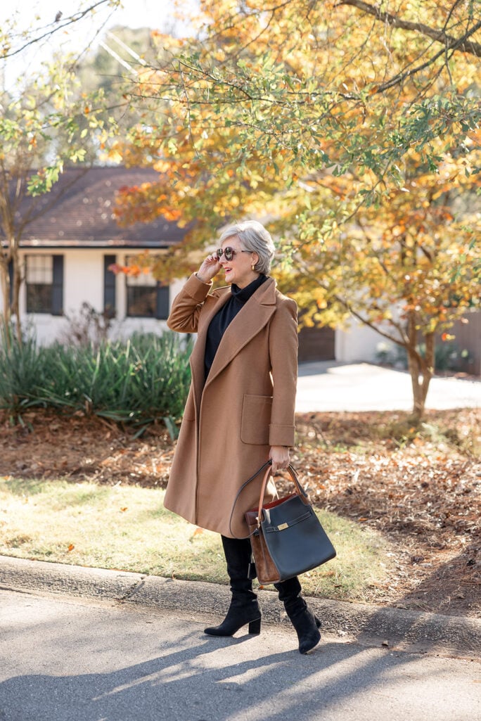 Beth wearing a camel coat, black sweater, and black heeled suede boots — sophisticated fall outfit idea for women 50 and up.