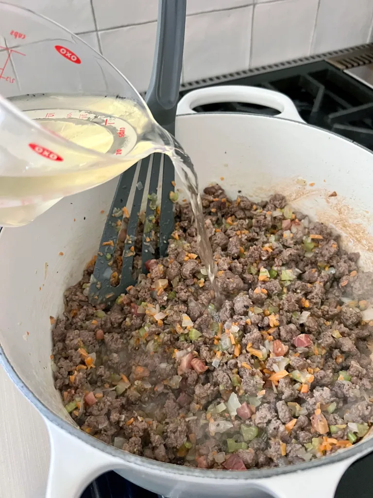 adding white wine to the ground lamb and soffritto mixture