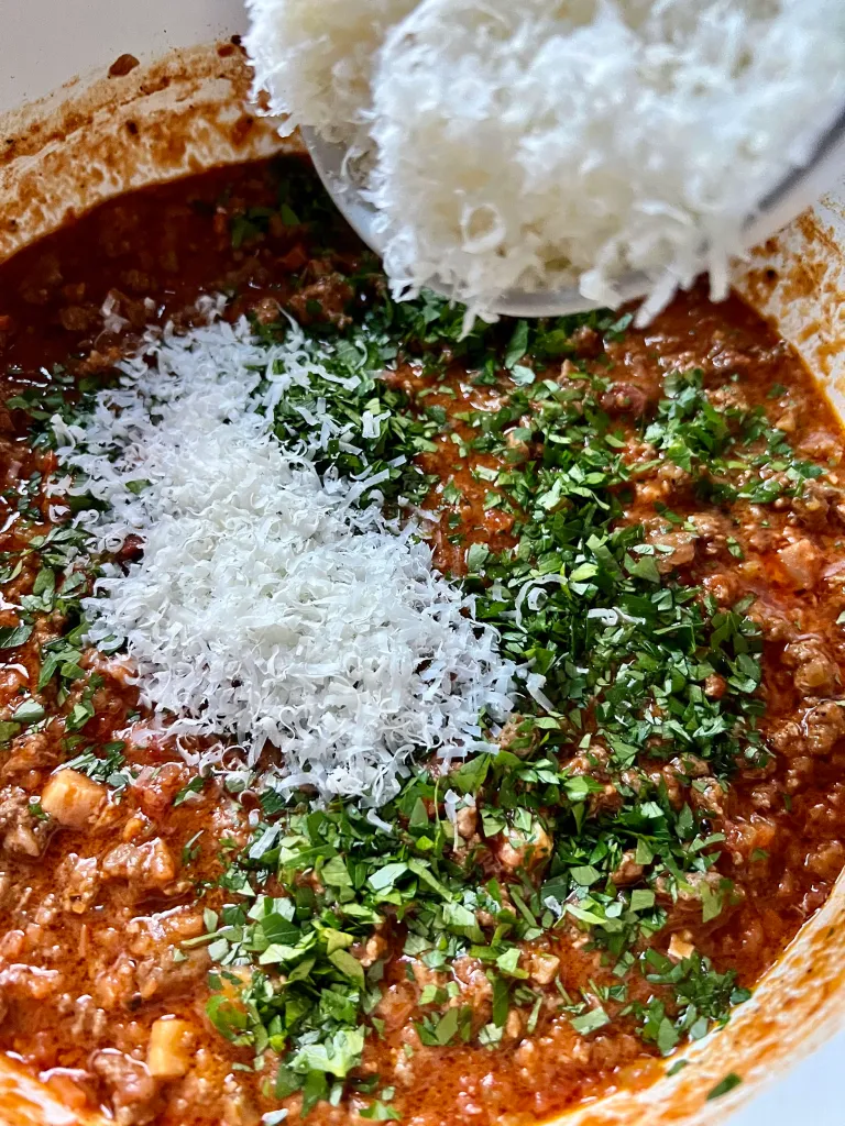 adding parmesan and parsley to the lamb bolognese