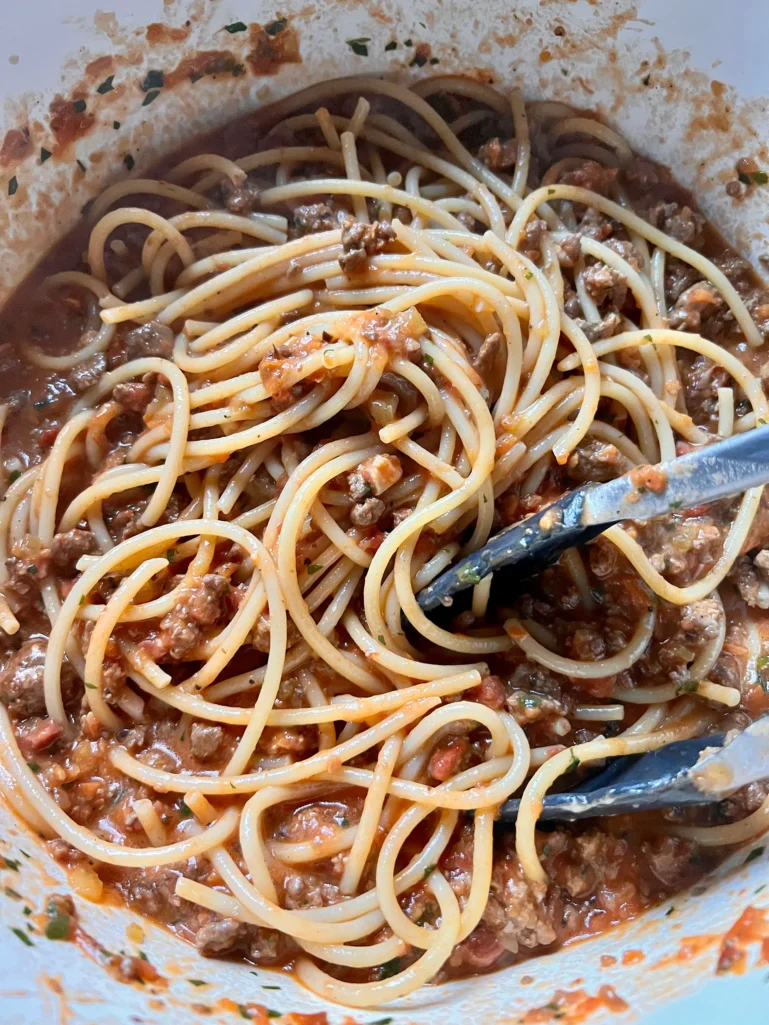 stirring bucatini pasta into bolognese