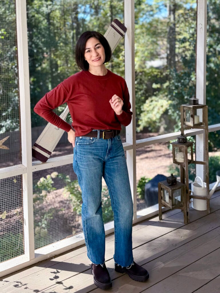 Kelly wearing a rust crewneck sweatshirt with rigid straight-leg jeans, a suede belt, and chunky Chelsea boots — casual fall weekend outfit for petites.
