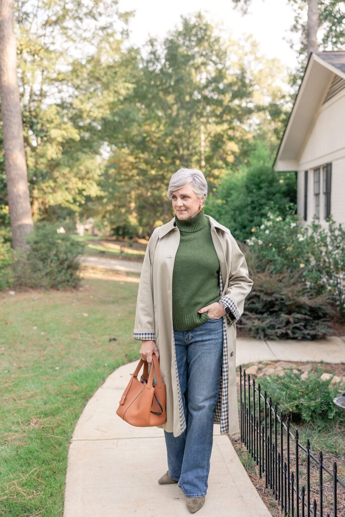 Beth wearing a green turtleneck sweater, jeans, and taupe suede ankle boots with a trench coat — casual, confident fall outfit for women over 50.