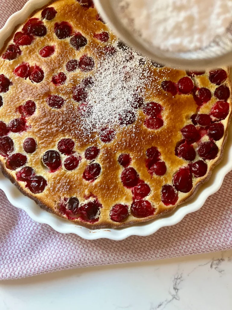 Dusting powdered sugar over freshly baked cranberry clafoutis
