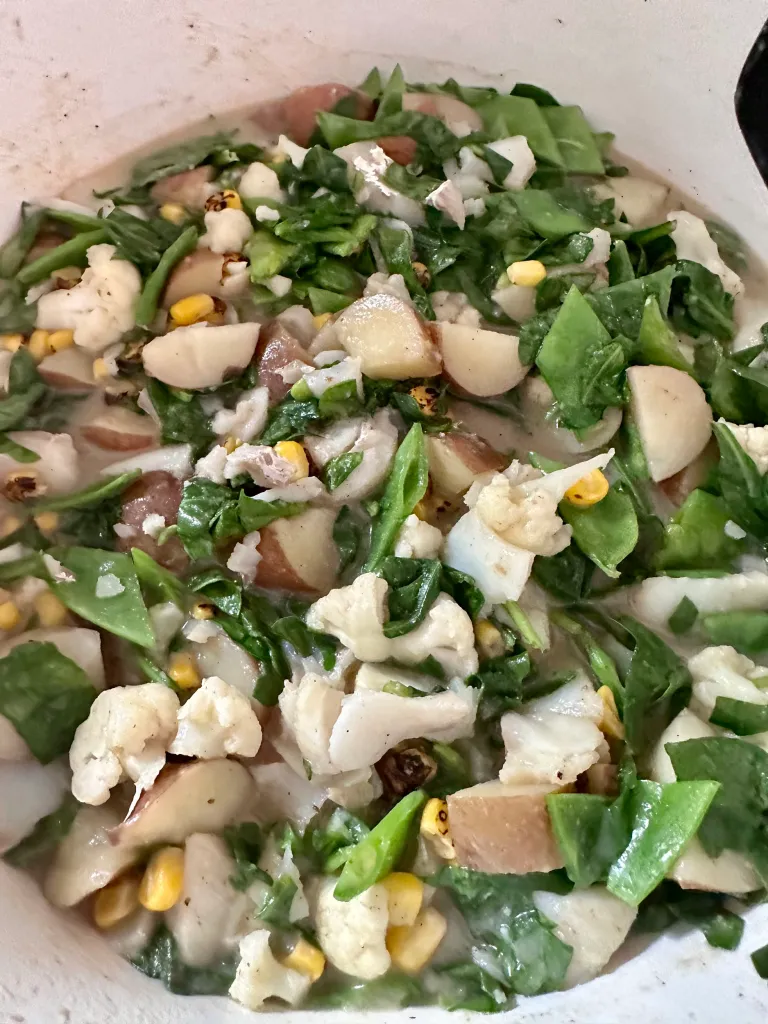 Adding chopped spinach, corn, and sliced snow peas to nearly finished dairy-free seafood chowder