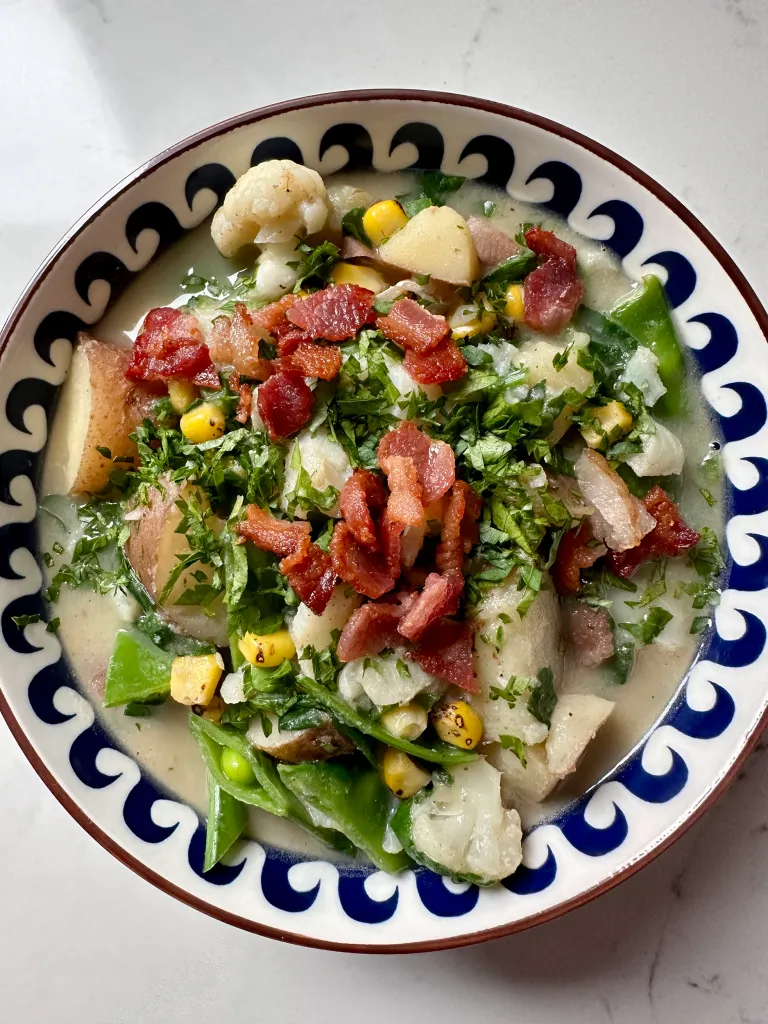 Finished bowl of dairy-free seafood chowder with cod, vegetables, bacon, and parsley in decorative blue and white bowl