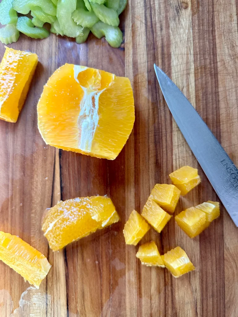Fresh orange cut and segmented on wooden cutting board with celery - prepping ingredients for lentil salad