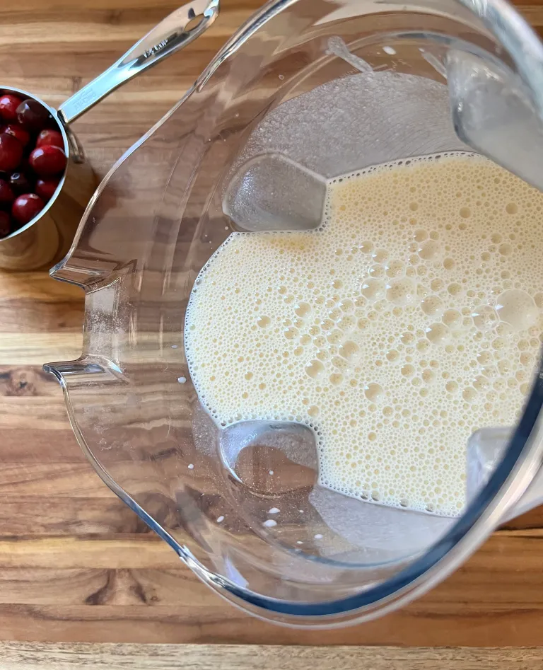 Smooth and creamy clafoutis batter in a blender with fresh cranberries nearby