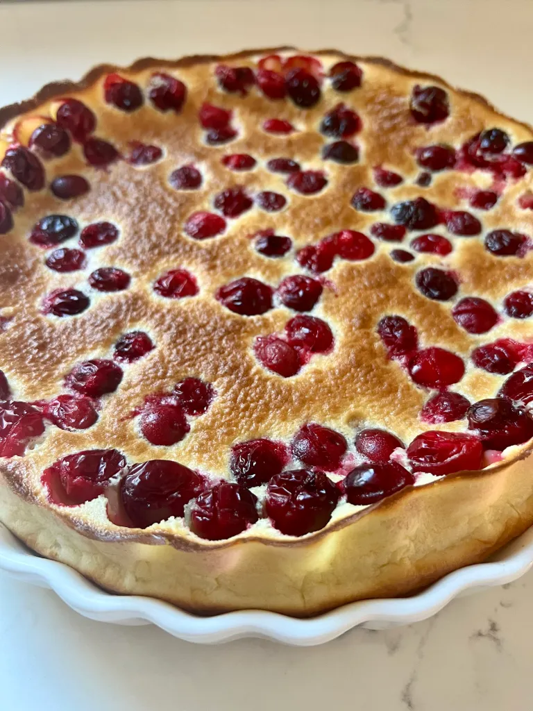 Golden brown cranberry clafoutis puffed and fresh from the oven in a white ceramic dish