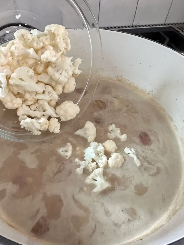 Adding fresh cauliflower florets to simmering dairy-free chowder with potatoes and creamy broth