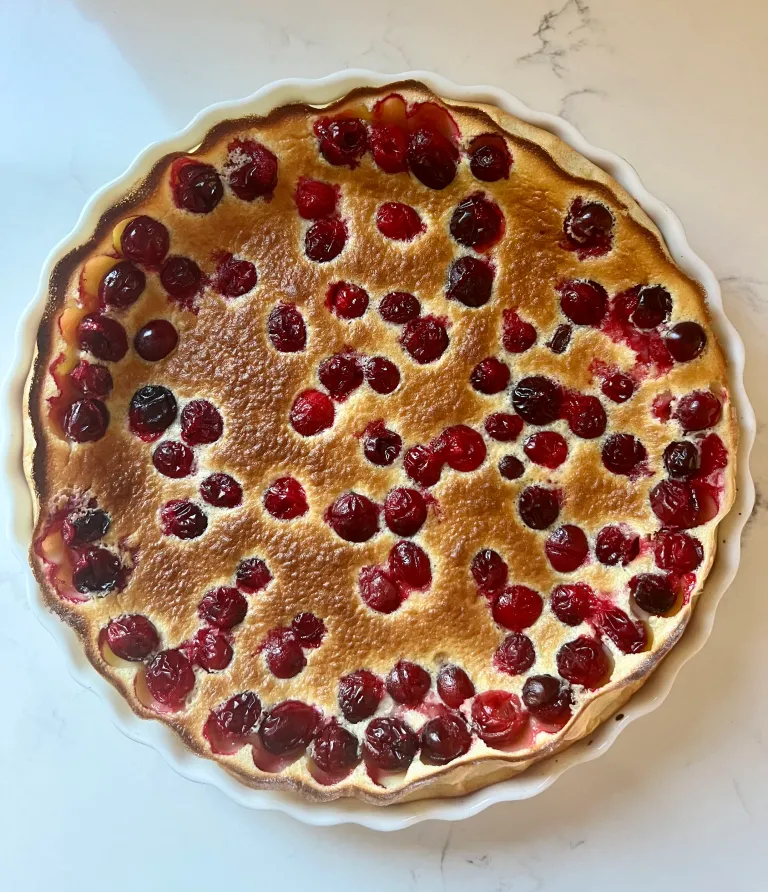 Overhead view of baked cranberry clafoutis with golden edges and bright red cranberries
