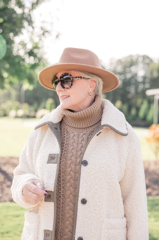 Beth Djalali wearing cream teddy shearling coat with camel turtleneck sweater and tan fedora hat - best winter coats for women over 50