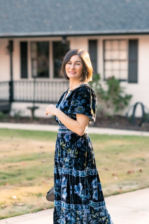 Kelly wearing navy blue floral velvet maxi dress with smocked waist, flutter sleeves, and crystal necklace - petite winter wedding guest dress