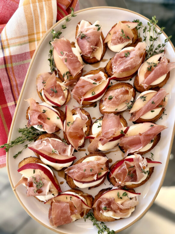 A platter of pear and prosciutto crostini with creamy cheese, fresh thyme, and a drizzle of balsamic glaze, perfect for cozy fall entertaining.