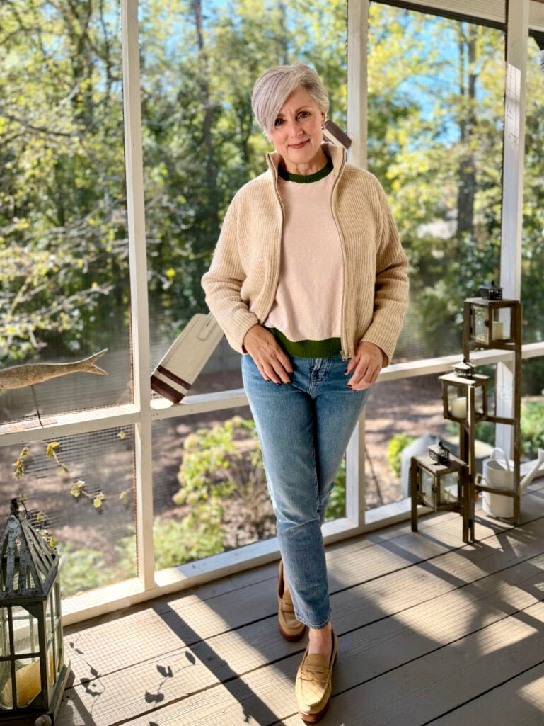 Beth wearing a neutral sweater layered over a green-trimmed top with jeans and suede loafers, the perfect casual sweater-weather outfit.