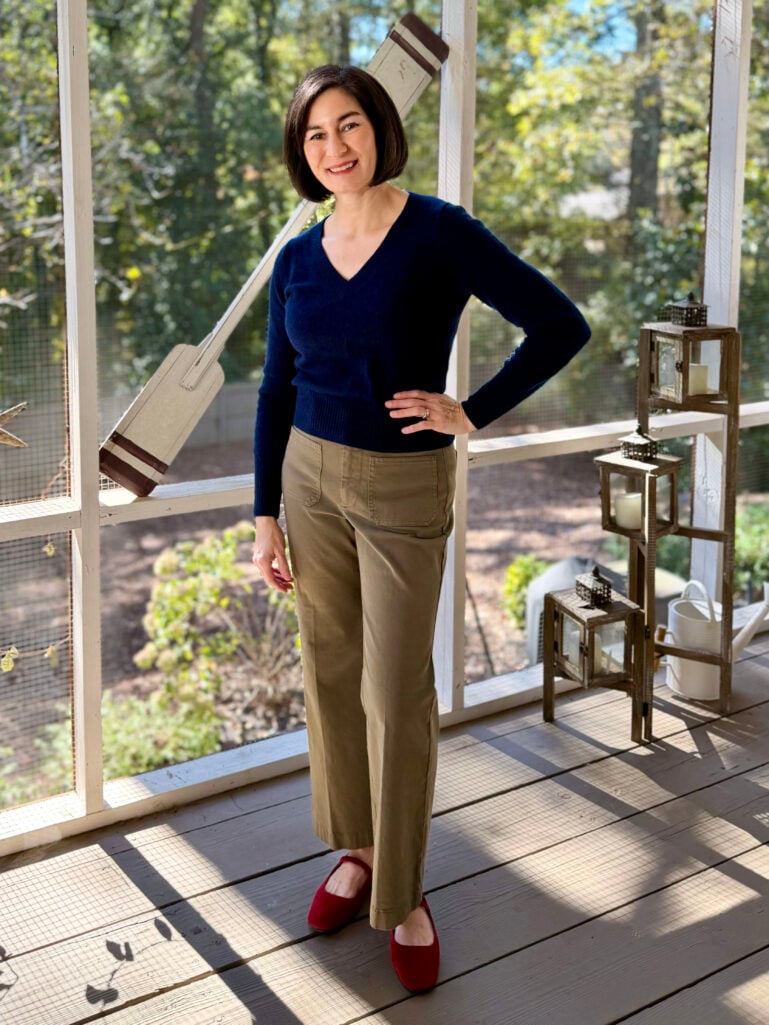 Kelly wearing a navy V-neck sweater with cropped olive chinos and red ballet flats—an effortless, chic fall outfit for casual entertaining.