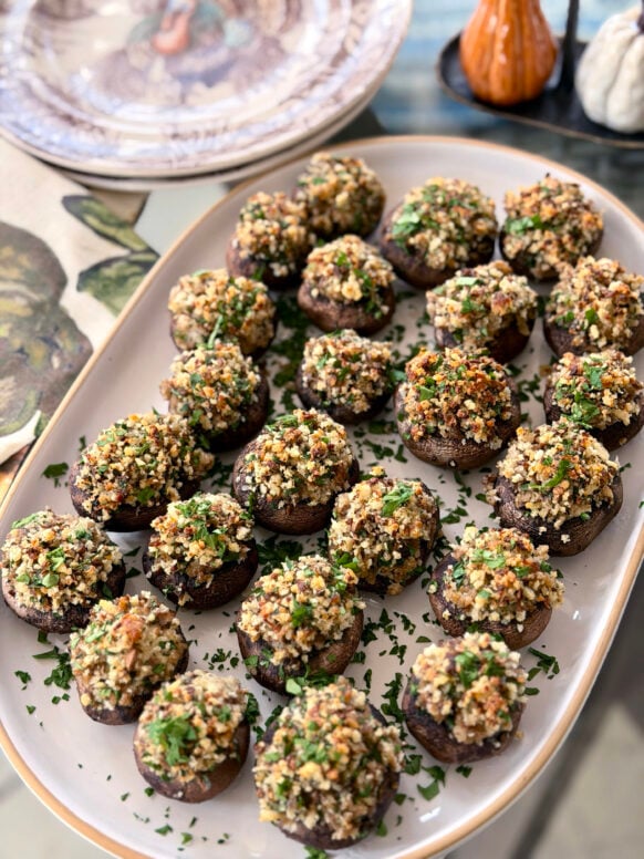 Close-up of golden-brown stuffed mushrooms with herb and breadcrumb topping arranged on a white serving platter, garnished with fresh parsley