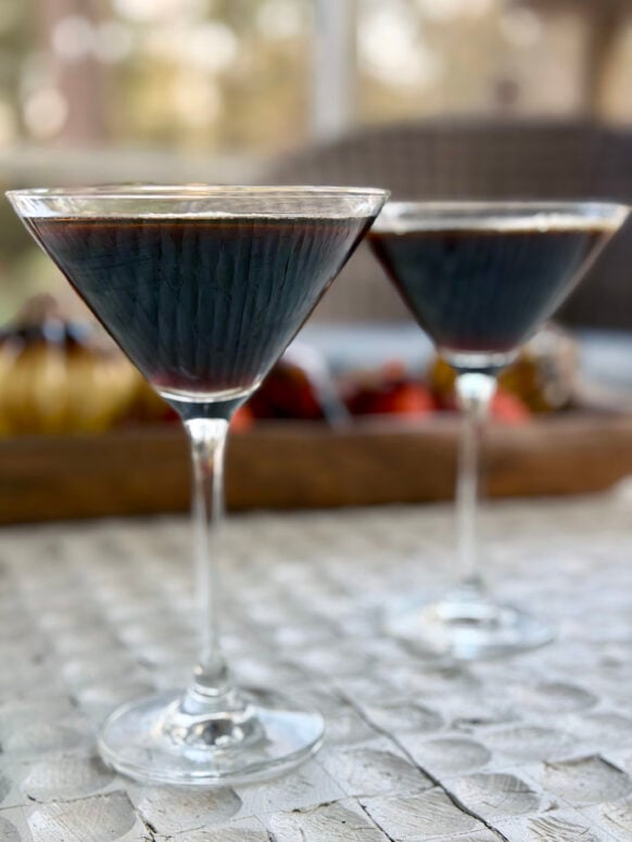 Two cinnamon espresso martinis in classic martini glasses with creamy foam tops, served on a marble surface with soft natural light