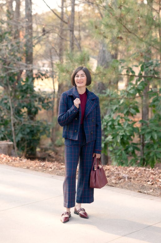 Kelly wearing navy windowpane plaid Maeve Colette suit with burgundy cashmere sweater, Mary Jane flats, and burgundy handbag in outdoor setting