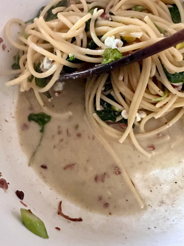 Stirring bucatini pasta with melting blue cheese and pasta water creating creamy sauce