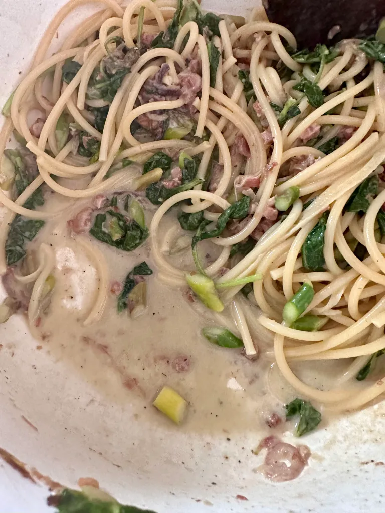 Blue cheese pasta sauce thickening around bucatini with asparagus and kale visible