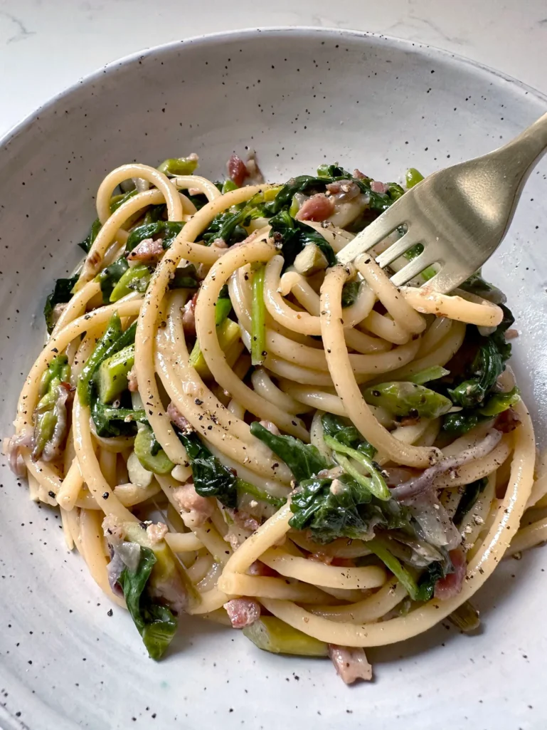 Close up of blue cheese bucatini with visible asparagus, kale, and pancetta on fork