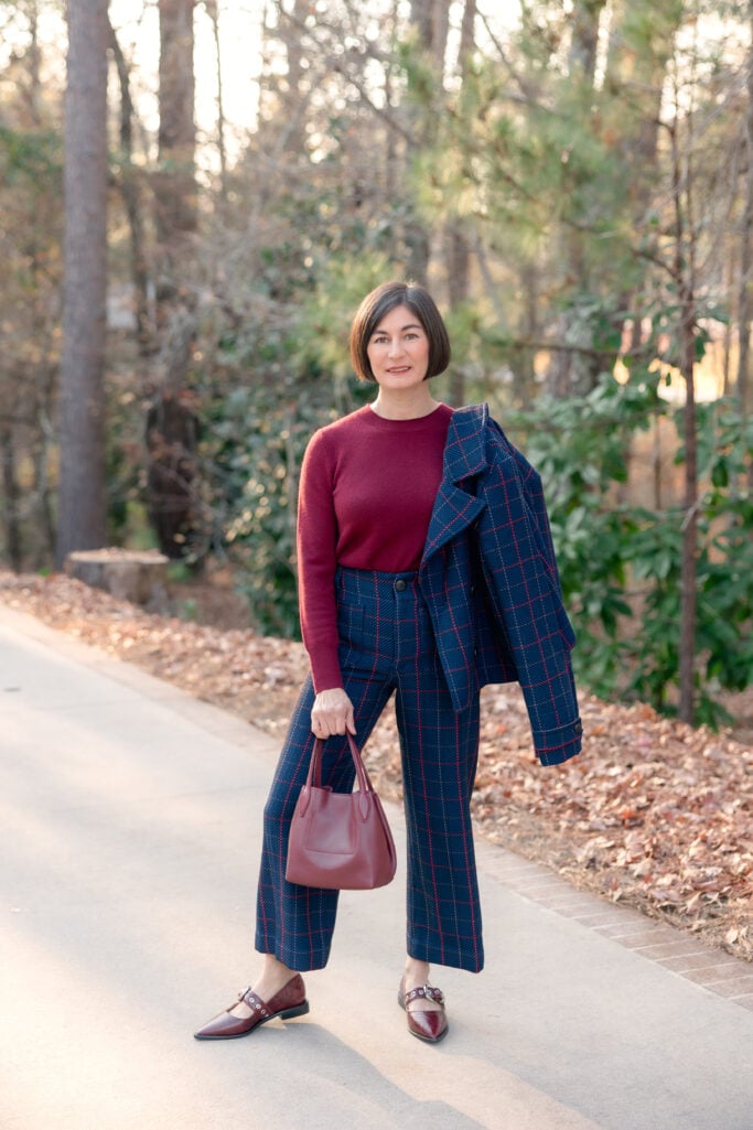 Kelly modeling burgundy cashmere crewneck sweater with Maeve Colette navy plaid cropped pants and Mary Jane flats, holding plaid blazer, showing alternative styling without jacket