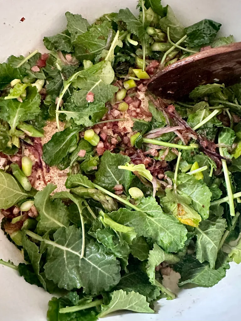 Fresh baby kale being added to pot with pancetta, onions, and asparagus