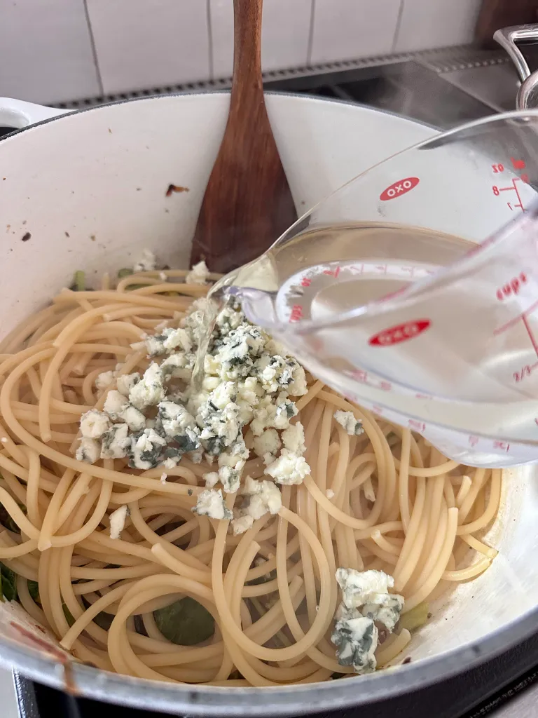 Pouring reserved hot pasta water over Roquefort cheese and bucatini