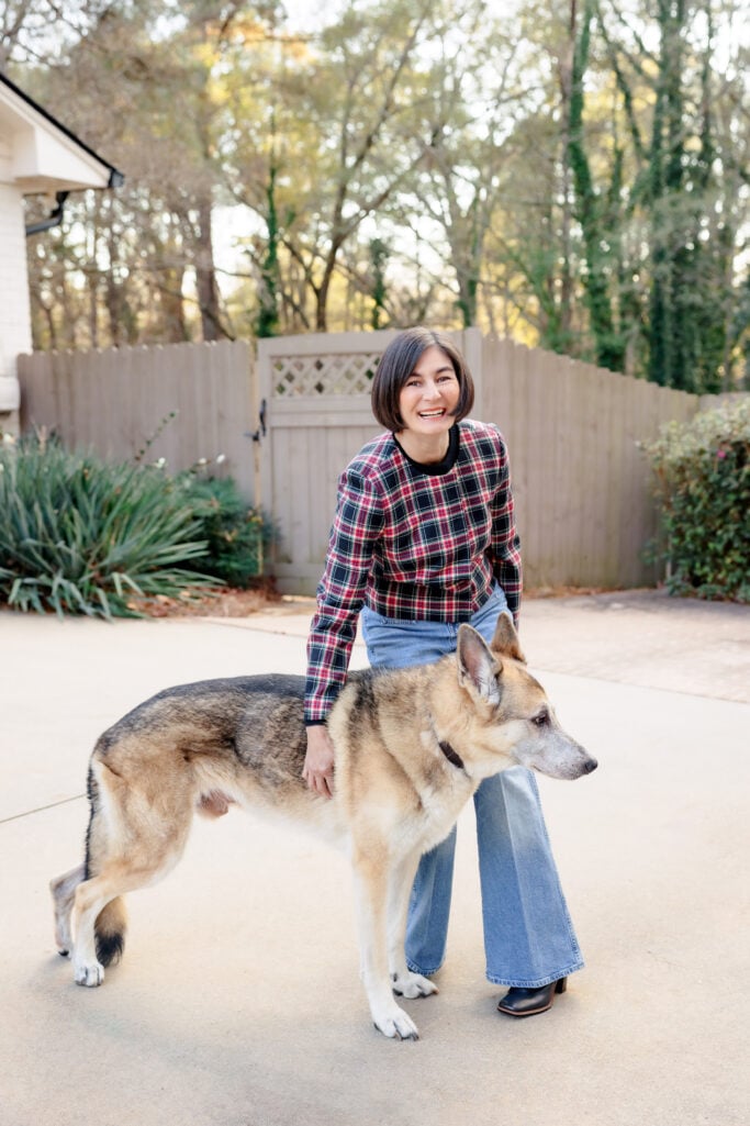 Kelly kneeling with dog wearing Stewart tartan plaid jacket and vintage flare jeans showing casual approachable holiday outfit for petites
