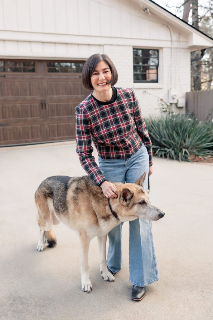 Kelly kneeling with dog wearing Stewart tartan plaid jacket and vintage flare jeans showing casual approachable holiday outfit for petites