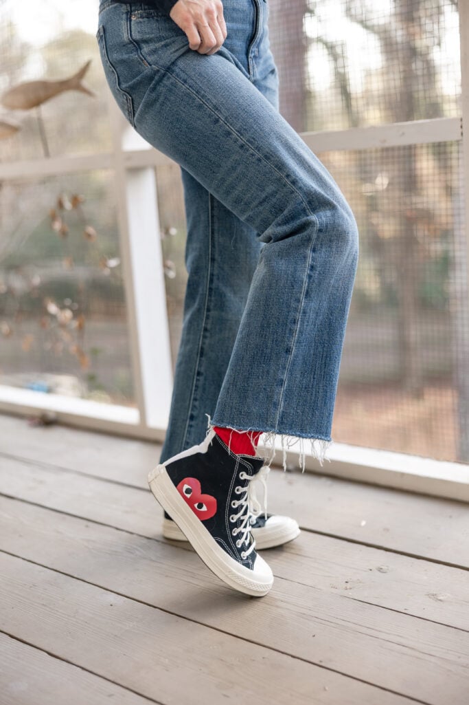 Close-up of Kelly's raw-hem jeans and Comme des Garçons PLAY x Converse high tops with signature red heart logo