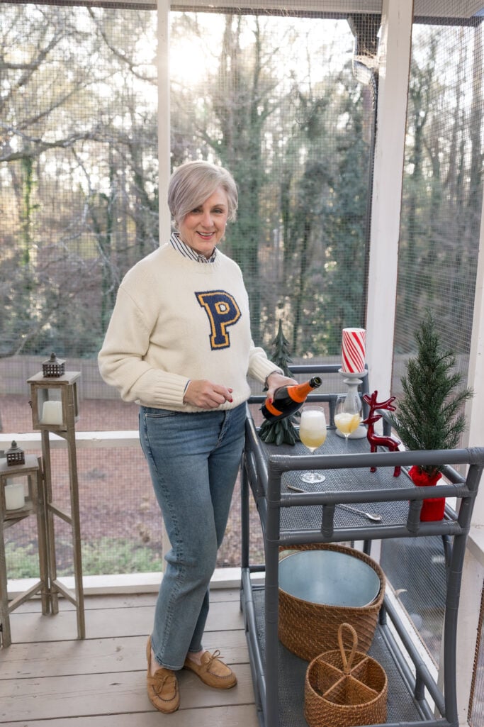 Beth pouring Mionetto Prosecco at the bar cart on the screened porch, surrounded by holiday decorations including a candy-striped candle and mini Christmas tree