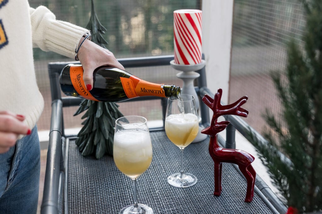 Close-up of Prosecco being poured into wine glasses over ice, with festive green tree and red reindeer decorations in the background