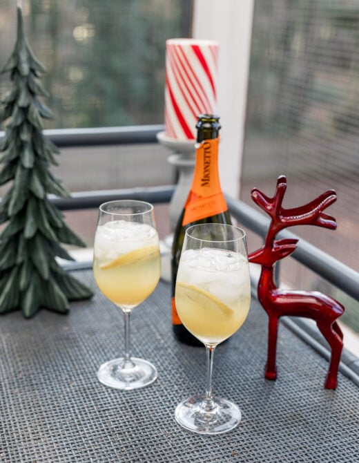 Two finished Prosecco punches garnished with lemon slices, Mionetto bottle and holiday decorations in the background