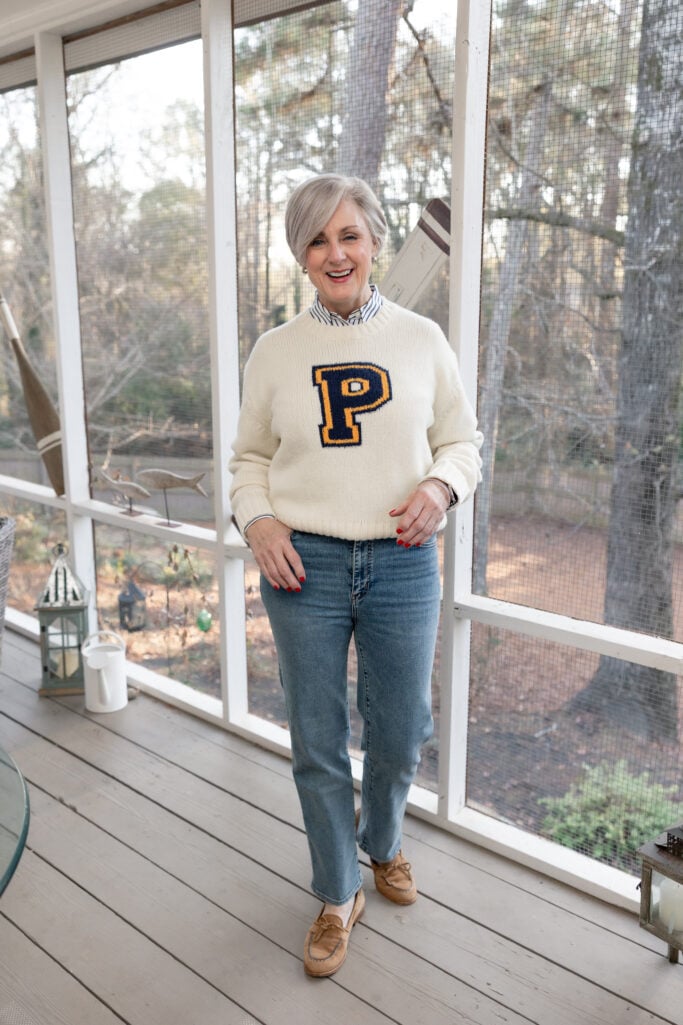 Full-length view of Beth in her Polo Ralph Lauren P sweater layered over stripes, with straight jeans and camel loafers on the screened porch