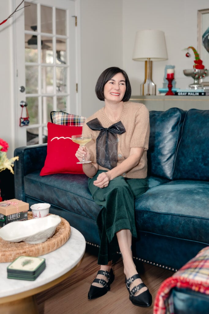 Woman over 50 wearing embellished bow-front cardigan with green corduroy pants and black pointed toe Mary Jane flats for a cozy New Year's Eve outfit