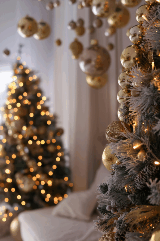 Cozy holiday scene featuring two Christmas trees decorated with gold ornaments and warm string lights, with frosted branches and hanging baubles creating a soft, glowing atmosphere.