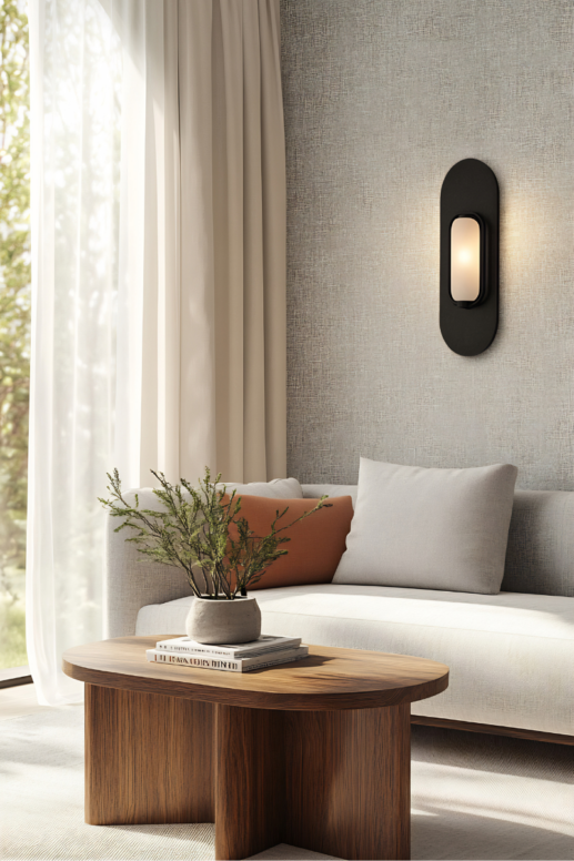 Serene living room with a light upholstered sofa, sheer curtains, and a sculptural wood coffee table styled with books and greenery, illuminated by a modern wall sconce for a calm, elevated home aesthetic.