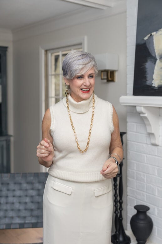 Woman over 50 wearing winter white sleeveless turtleneck and skirt with gold chain necklace