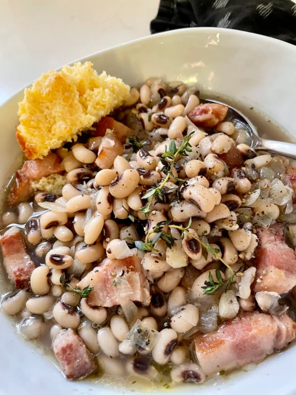 Bowl of black-eyed peas with bacon and fresh thyme served with a piece of cornbread on the side