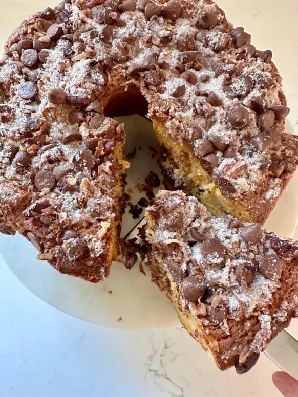 Chocolate cinnamon coffee cake with streusel topping dusted with powdered sugar on a white cake stand with a slice removed