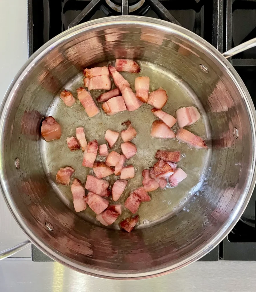 Cubed slab bacon browning in a stainless steel pot