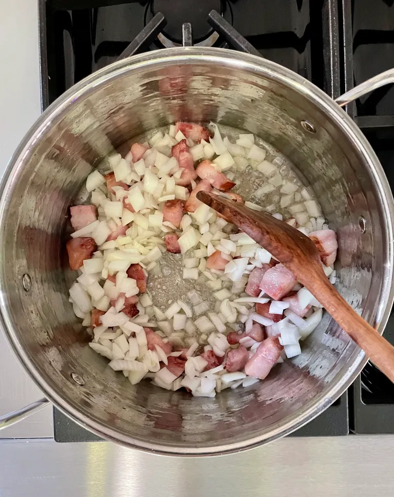 Diced onions cooking with bacon pieces in a pot with a wooden spoon