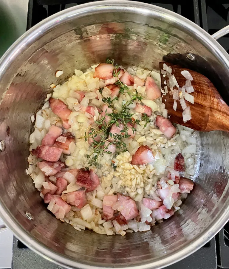 Fresh thyme sprigs and chopped garlic added to bacon and onion mixture in pot