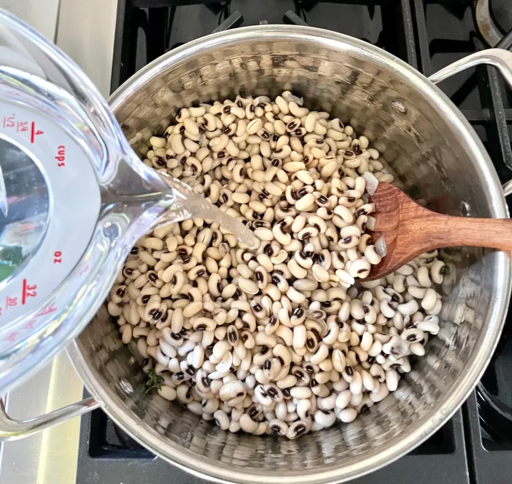 Water being poured from a measuring cup into pot of black-eyed peas