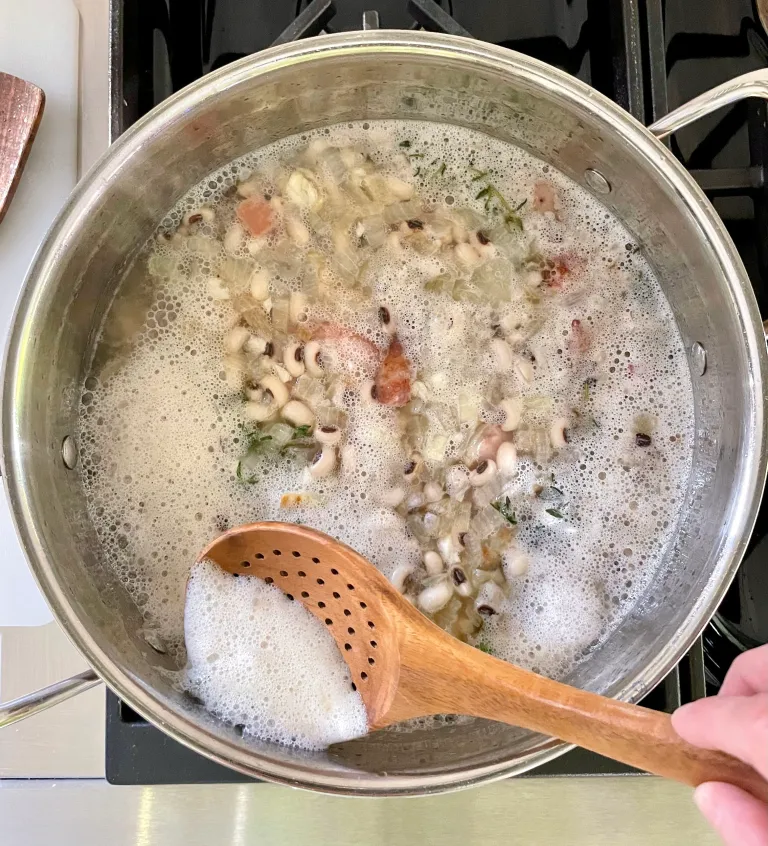 Skimming foam from simmering black-eyed peas with a wooden slotted spoon