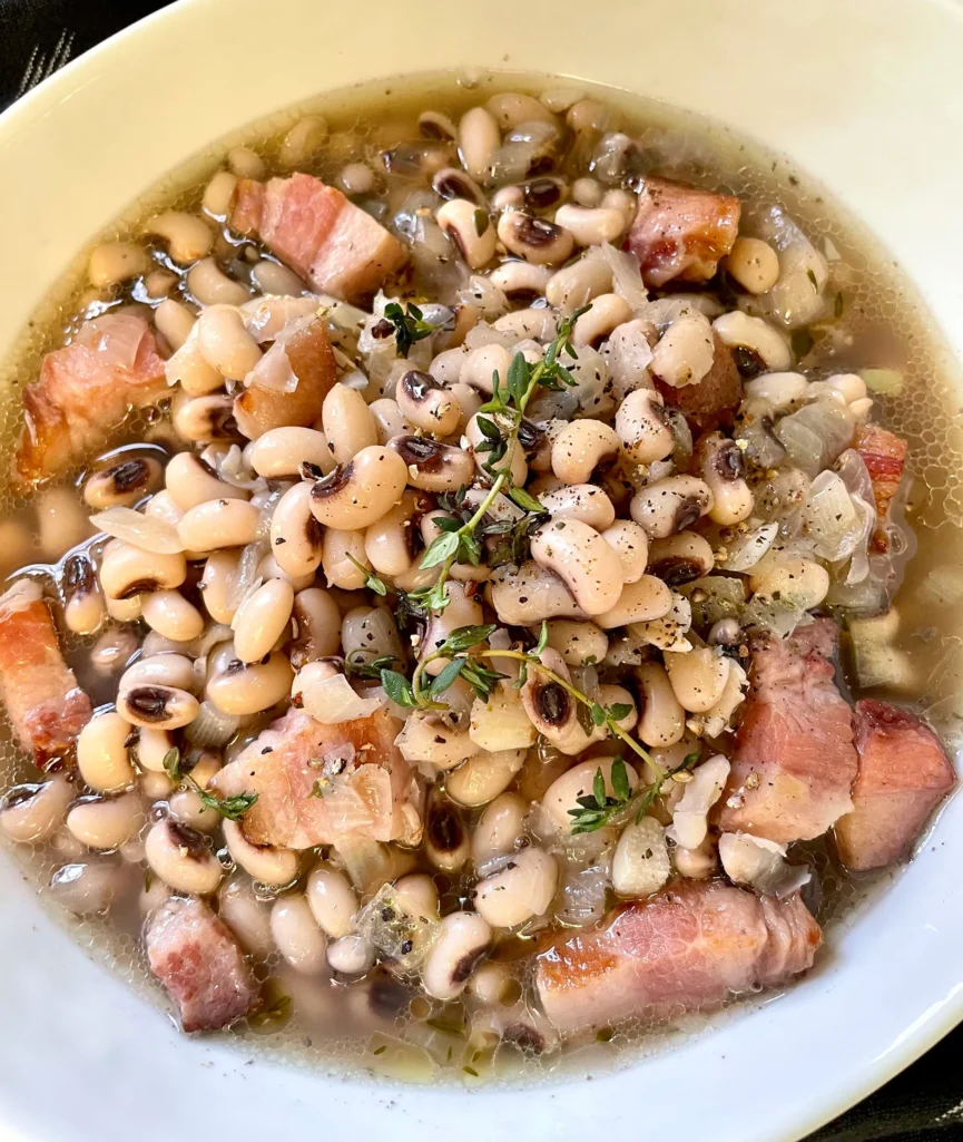 Bowl of black-eyed peas with chunks of bacon in savory broth topped with fresh thyme