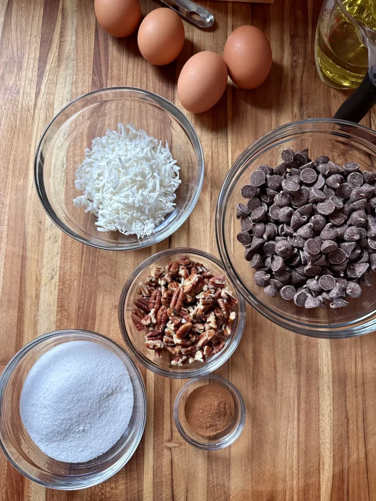 Streusel ingredients in glass bowls: chocolate chips, shredded coconut, chopped pecans, sugar, and cinnamon