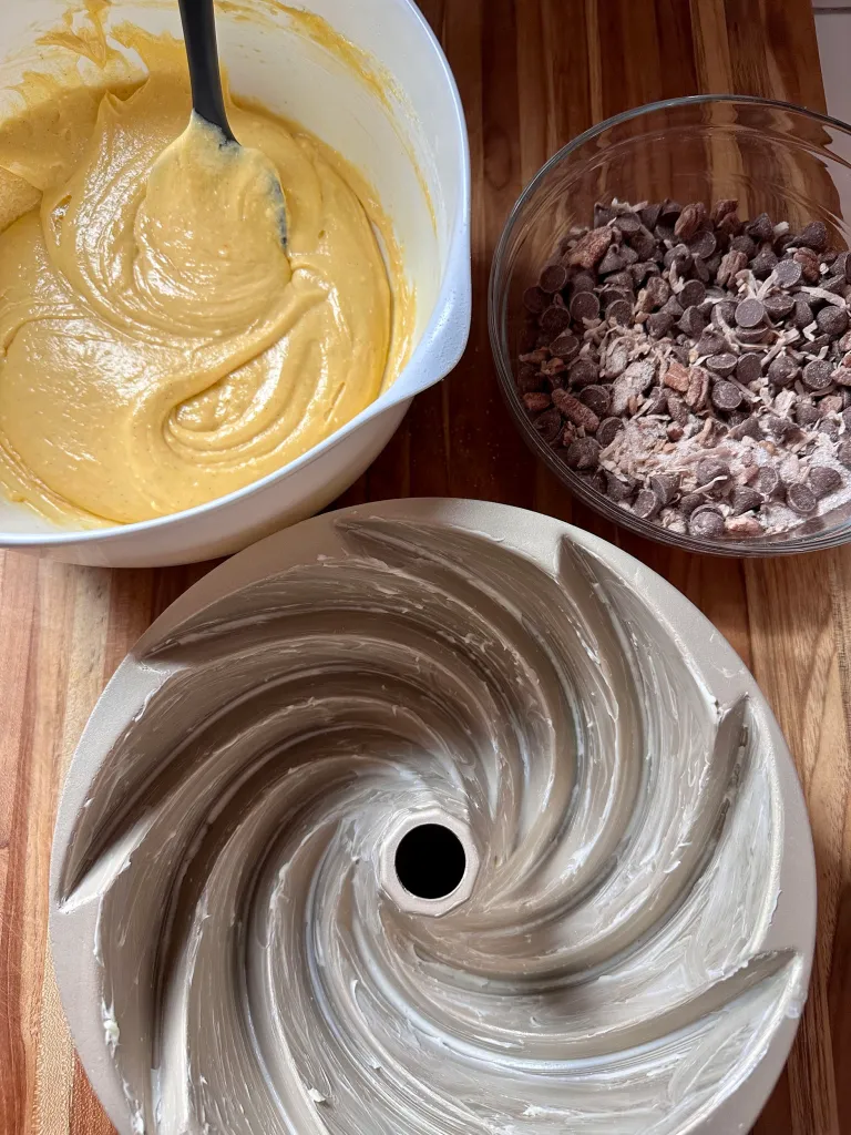 Smooth yellow cake batter next to a buttered bundt pan and streusel mixture