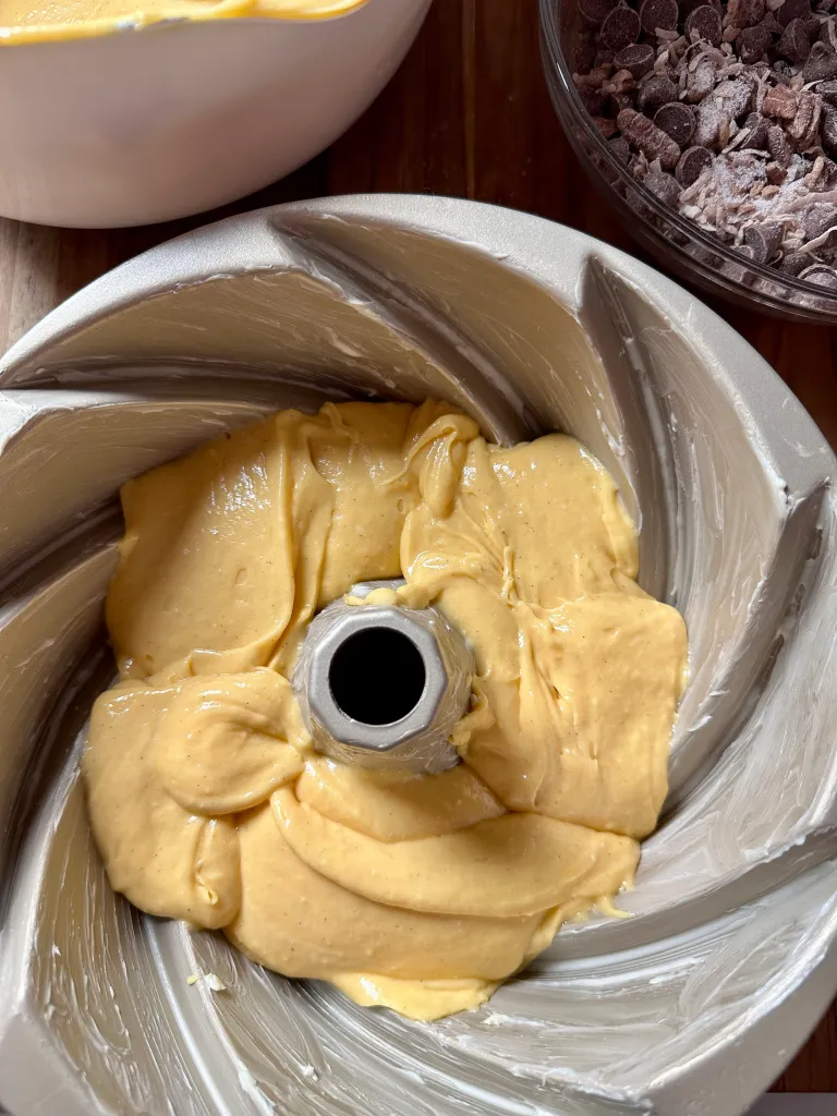 Pouring half of the yellow cake batter into a buttered bundt pan